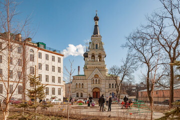 Obraz premium Bright, April, Sunday morning in the square against the background of the church and playground, where children play under the care of their parents