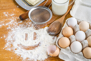 board for baking dough on it a smiley face made of flour. various ingredients and baking utensils.