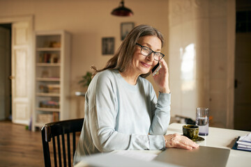 Horizontal image of beautiful retired woman copywriter working from home sitting at desk with...