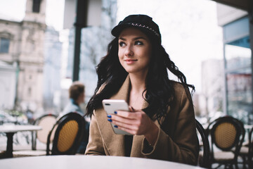 Cheerful young woman using smartphone in street cafe in cold day