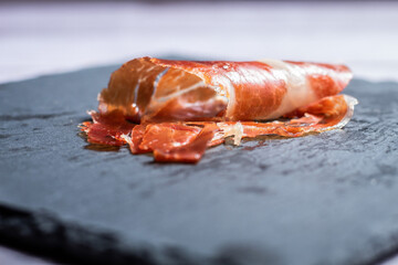 Jamón ibérico en un primer plano encima de una pizarra negra bien presentado