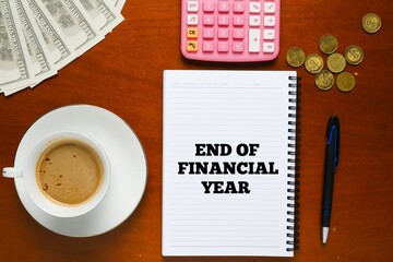 Flatlay picture of note book with end of financial year word, pen, fake cash, coins and calculator.