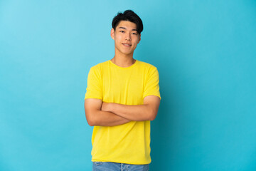 Young Chinese man isolated on blue background keeping the arms crossed in frontal position
