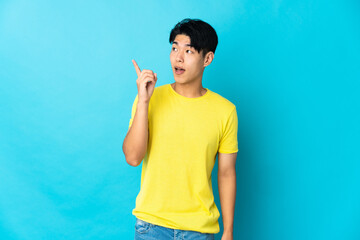 Young Chinese man isolated on blue background intending to realizes the solution while lifting a finger up