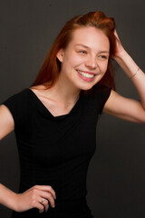 portrait of a young red-haired woman in a black dress. Studio photo on a black background.