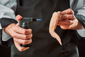 Man using a blow torch to roast chicken wing for crispy skin - Powered by Adobe
