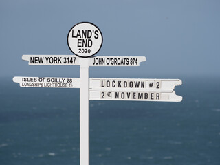 Iconic signpost at Land's End in UK has 'Lockdown 2' written on it indicating current affairs in UK Coronavirus epidemic restrictions.Sea in background © Tony Skerl
