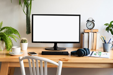 Modern office desk with blank monitor screen of computer on wooden office desk and mock up. White wall, book, clock, coffee, pencil and notebook in interior of workplace room. Business, work online.