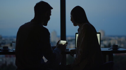 Silhouette of relaxed couple watching video on mobile phone in office.