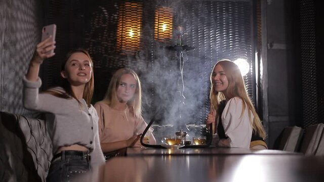 A group of young girls smoke a hookah and exhale white smoke.