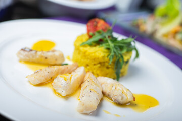 Fillet of white fish in sauce on a plate with garnish and herbs.