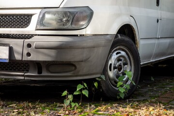 The frontal part of old white van parked for years at parking lot with grass growing around. Wreck on a public road.