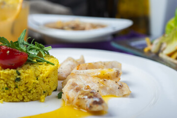 Fillet of white fish in sauce on a plate with garnish and herbs.