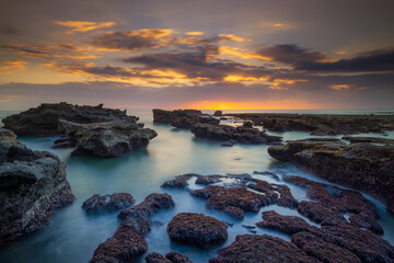 Beautiful seascape. Long exposure rocky beach during low tide. Panoramic ocean view. Composition of nature. Sunset scenery background. Cloudy sky. Water reflection. Mengening beach, Bali