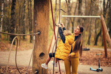 beautiful little girl climbs the rope park. sportswear modern brave girl. mom and daughter have fun together. autumn fashion