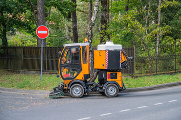 Street sweeper machine on the road against the background of a fence and dense forest, next to the...