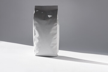 Blank white foil pouch bag on grey background in minimal style with natural harsh shadows....
