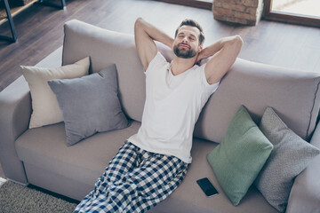 Top above high angle view photo of cheerful satisfied man sit divan sleep stretch hands enjoy rest relax wear checkered plaid pants trousers in living room indoors