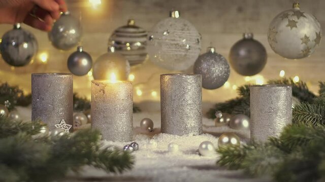 Footage of elegant advent decoration with fir branches on snow and four candles being lit, with lights and baubles hanging in the background