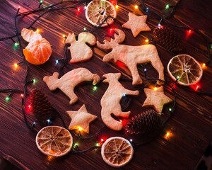 Christmas still life close up of gingerbread cookies surrounded by citrus, cones, christmas lights on a dark wood table. Festive background. Happy Holidays and New Year greeting card, frame. Noel