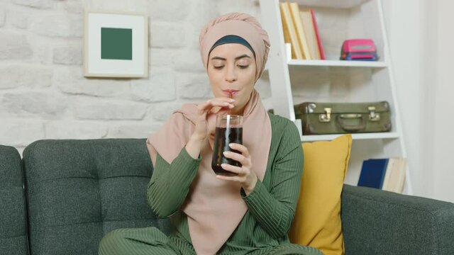 Young muslim woman drinks black cola In home.Slow motion video.