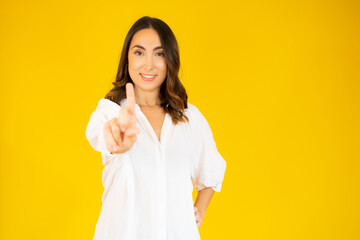 Portrait of a happy young woman pointing fingers up at copy space isolated over yellow background