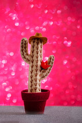 The toy potted cactus cowboy in hat with flower is on pink gradient glitter sparkle background. The concept of Live humanized toys, party invitation.