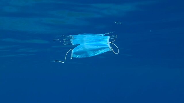 Discarded medical face mask slowly drifts under surface of  the blue water in sunlight.  