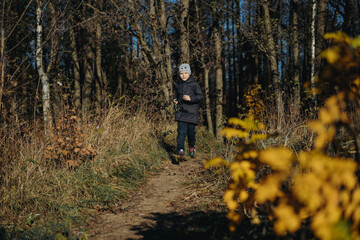 Obraz premium 7 years old caucasian school boy running along the footpath in autumn forest on sunny october day. Image with selective focus