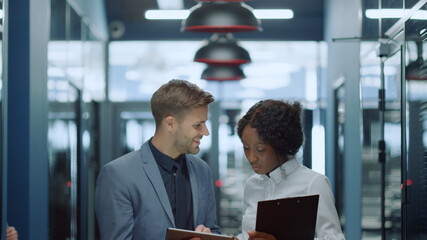 Positive business couple using tablet in corridor. Colleagues discussing project