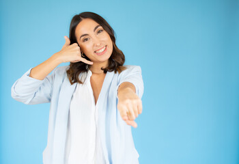 Portrait of attractive happy woman gesturing with fingers call me over blue background.