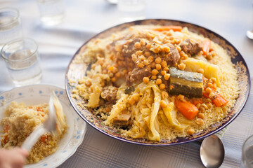 Traditional Moroccan homemade Couscous plate on a blue squared clothed table being served with glasses spoons and water . Morocco traditional family gathering concept.