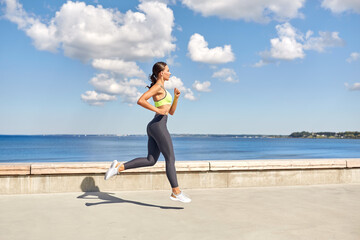 fitness, sport and healthy lifestyle concept - young woman running along sea promenade