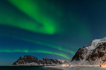 Obraz na płótnie Canvas Spectacular dancing green strong northern lights over the famous round boulder beach near Uttakleiv on the Lofoten islands in Norway on clear winter night with snow-clad mountains