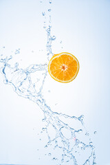 Fototapeta na wymiar Half of orange fruit with water splash in midair, isolated on light blue background
