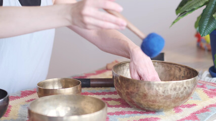 Woman playing on Tibetan singing bowl while sitting on yoga mat. Vintage tonned.