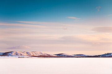 Snow-covered ice on the frozen lake at sunset. Beautiful winter landscape. Bannoye lake in South Ural, Russia