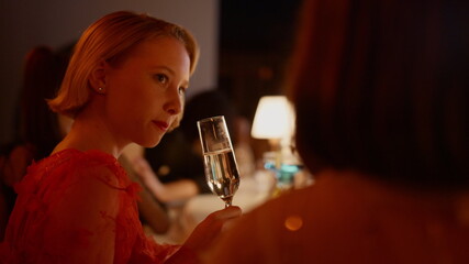 Beautiful girl drinking champagne in bar. Lady speaking with friend in nightclub