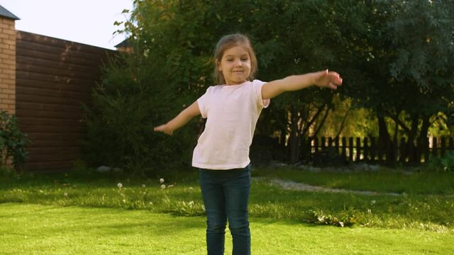 Little Caucasian beautiful girl depicts the plane with her arms outstretched to the sides like wings. Positive emotions, non-verbal gestures. Everyday leisure