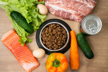 Dry pet dog food with natural ingredients. Raw meat, fish, vegetables, eggs and salad near bowl...