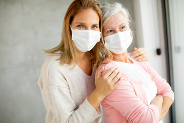 Senior woman with caring daughter at home wearing medical masks