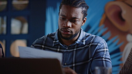 Upset afro man throwing paper in coworking. Man crumpling document in office