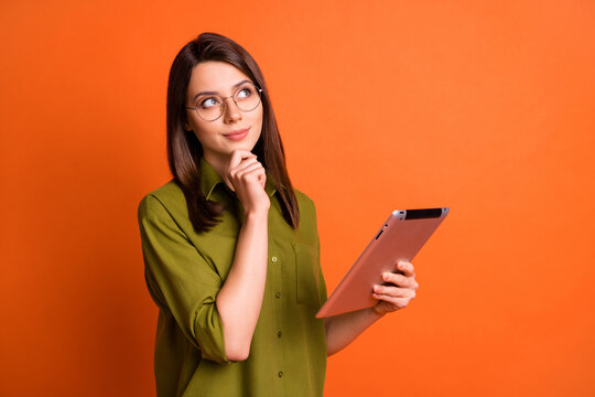 Photo portrait of dreamy brunette student thinking about idea keeping tablet isolated on bright orange color background