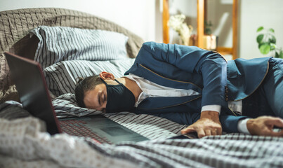 Businessman in suit and mask is sleeping in bed next to laptop. Fatigue and exhaustion from hard...