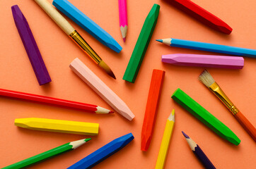 Top view of wax pencils, classic pencils, brushes for painting on the orange background