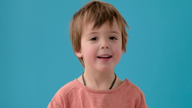 Adorable little boy in orange t-shirt shakes head in disbelief posing for camera at bright turquoise studio wall closeup