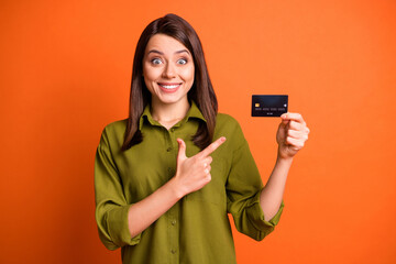 Photo portrait of young girl staring showing at debit card smiling isolated on bright orange color...