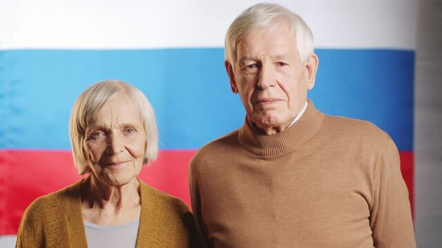 Portrait studio shot of cheerful senior man and woman looking together at camera while posing against Russian flag