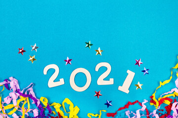 Año 2021, números en madera sobre un fondo azul liso y aislado junto a estrellas de colores y confeti. Vista superior. Copy space