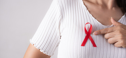Closeup of woman hand pointing to red badge ribbon on chest to support AIDS Day. Healthcare, medicine and AIDS awareness concept.